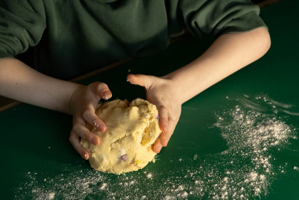Child's hands kneading dough on a green surface.
